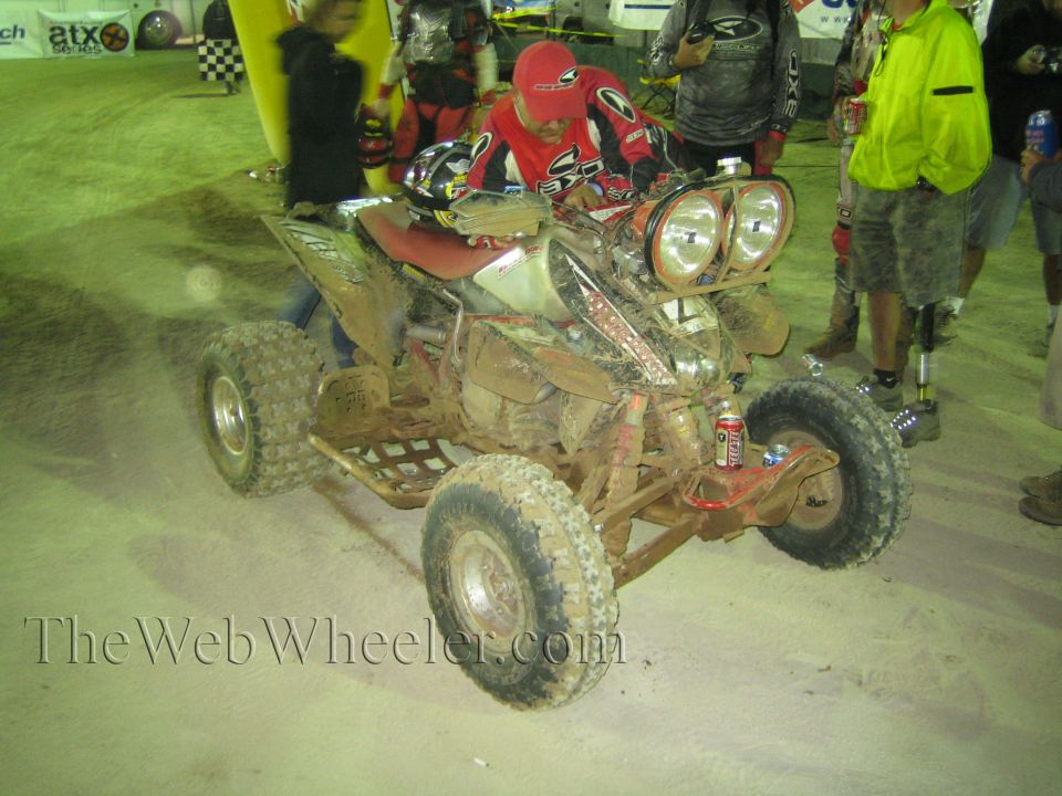 Mud-covered sport ATV with dual headlights and rider at night