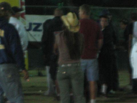 Group of people standing and talking at a fenced nighttime event