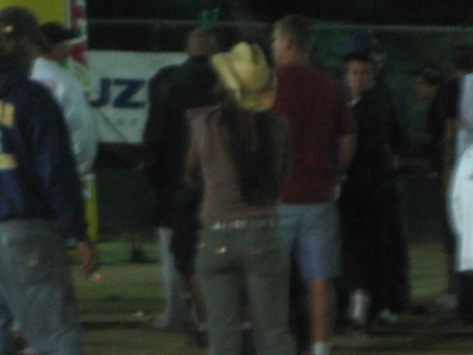 Group of people standing and talking at a fenced nighttime event