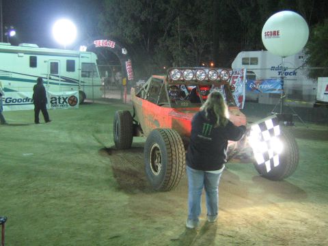 Red off-road buggy with light bar at night, person with checkered flag