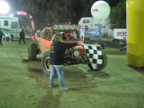 Orange off-road buggy with light bar at night, flagger with checkered flag
