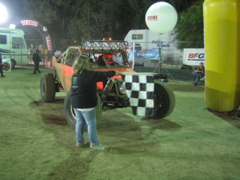 Orange off-road buggy at night with person waving checkered flag