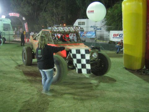Orange off-road buggy at night, flagger in Monster hoodie with checkered flag