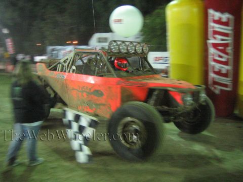 Orange off-road buggy with light bar at night near Tecate arch, person with flag