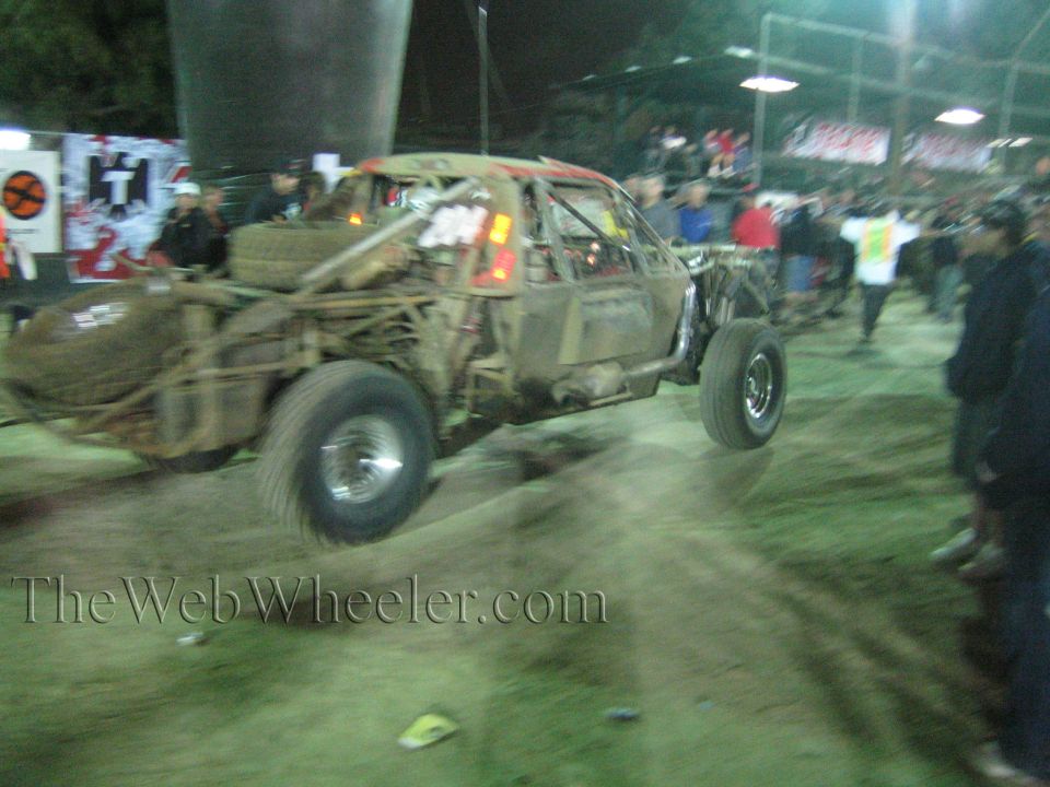 Mud-caked off-road race car number 117 driving through a crowd at a floodlit night event