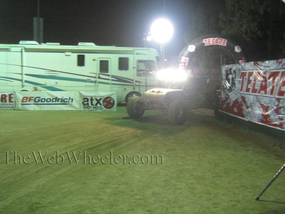 Off-road buggy with headlights on near Tecate arch and RV at a floodlit night event