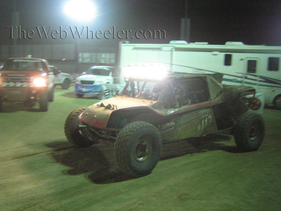 Off-road buggy with roof lights driving past pickups and RVs in a night paddock