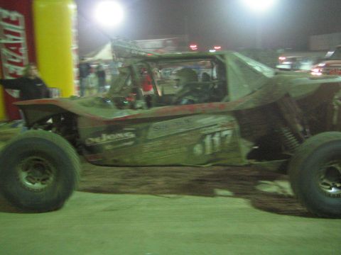 Side view of mud-spattered off-road buggy number 117 in motion at a night event