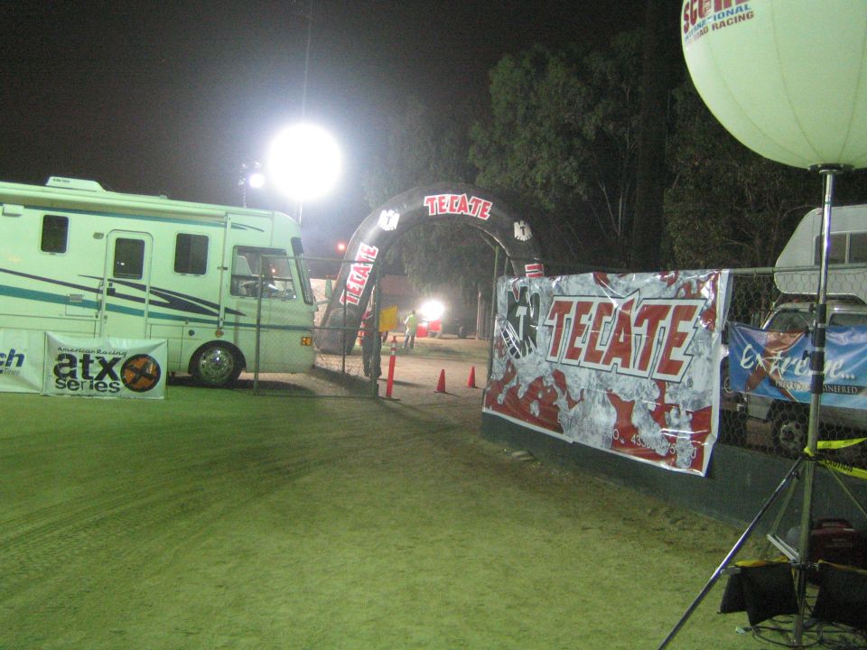 Glowing Tecate arch and banner beside an RV at a night off-road race venue