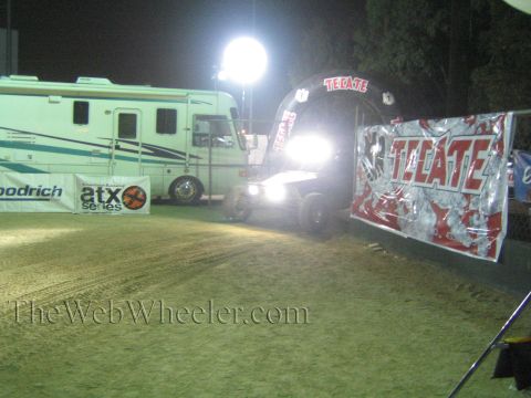 Off-road buggy with bright headlights entering a glowing Tecate arch at night