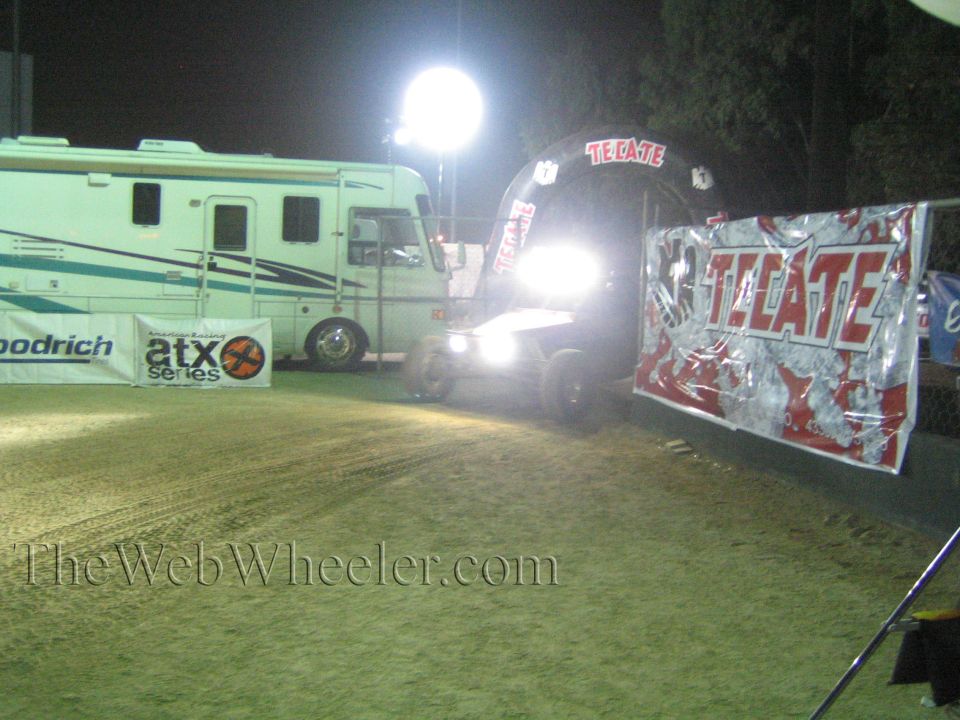 Off-road buggy with bright headlights entering a glowing Tecate arch at night