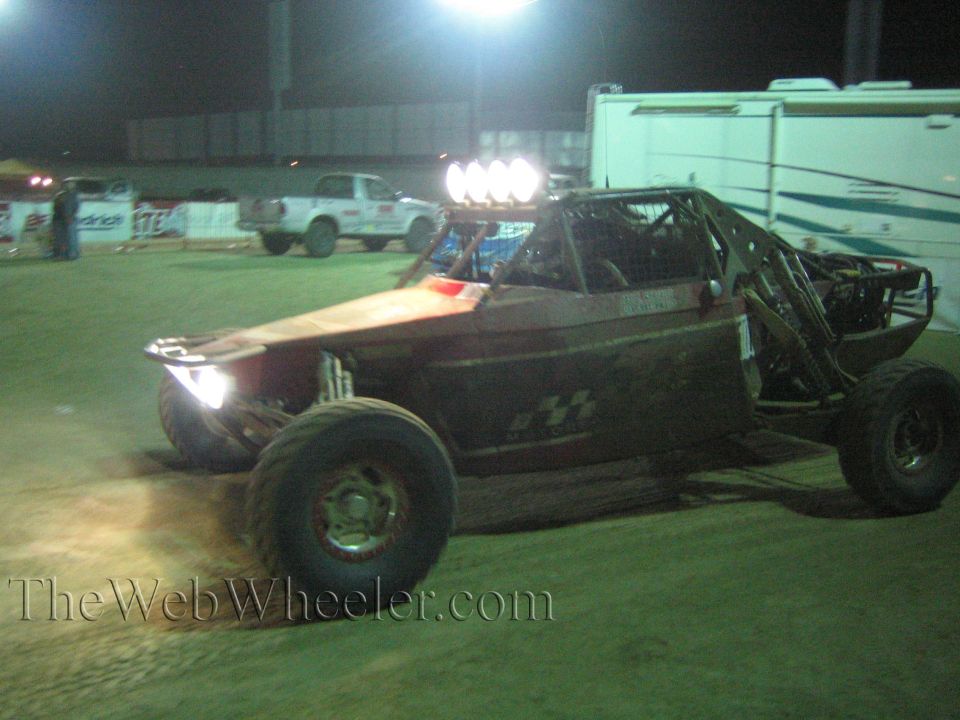 Dark off-road buggy with roof lights and headlight on driving in a night paddock