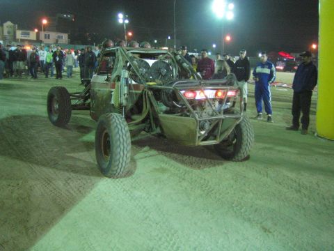 Tube-frame off-road buggy with glowing taillights amid spectators