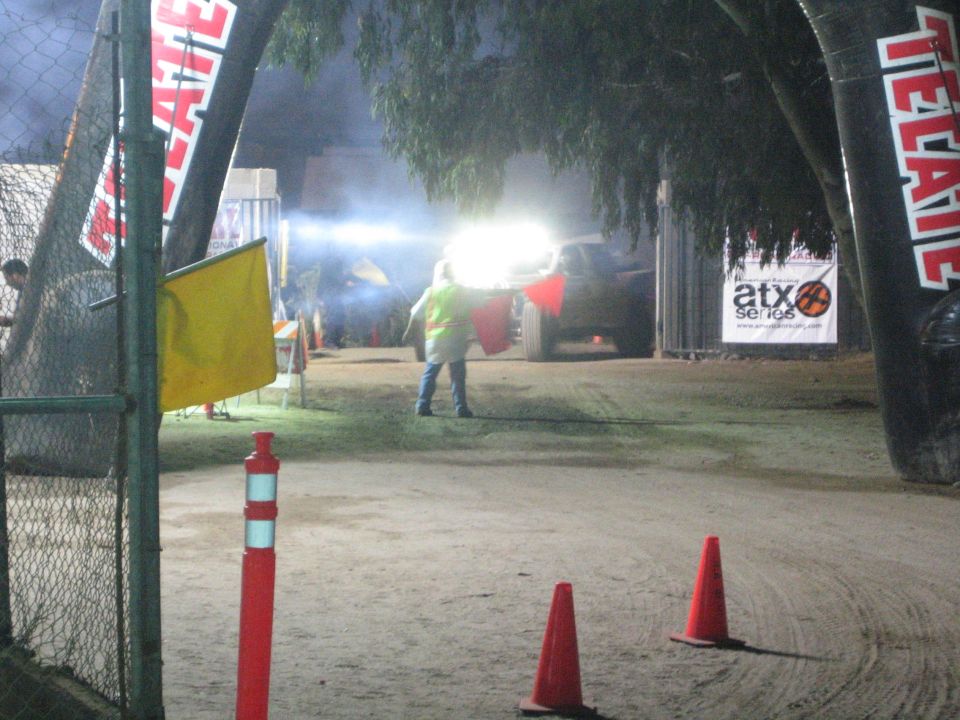 Course marshal in vest by a lit Tecate inflatable arch at night