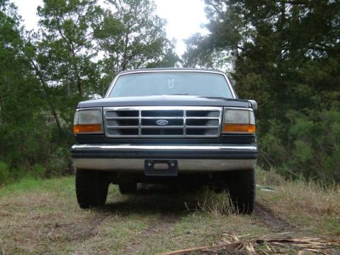 1992 Ford Bronco - Front view of a 1992 Ford Bronco with a chrome grille, parked outdoors on a dirt path.