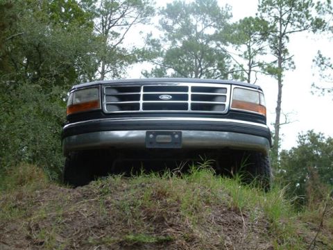 1992 Ford Bronco - The front grille and headlights of a 1992 Ford Bronco are visible as it sits on a dirt and grass hill.