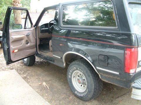 1992 Ford Bronco - The driver's side door of a black 1992 Ford Bronco is open, revealing the interior and part of the front wheel.