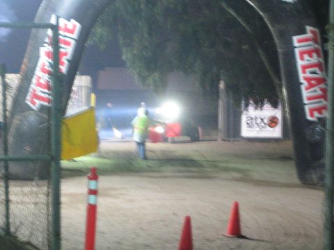 Marshal in hi-vis vest at a dirt course under Tecate arch at night