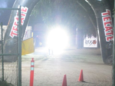 Bright headlight glare at a dirt course under Tecate arches at night