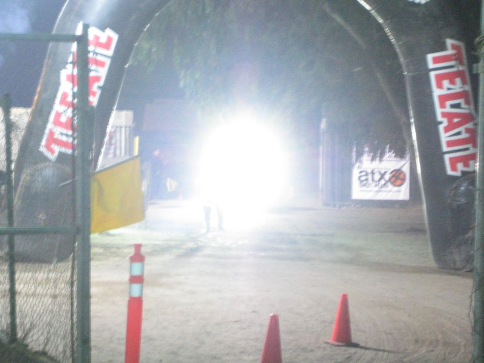 Bright headlight glare at a dirt course under Tecate arches at night