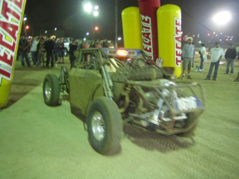 Front view of a tube-frame off-road buggy by a Tecate arch at night