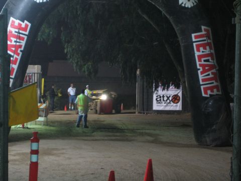 Vehicle with headlights at a dirt course under Tecate arch at night