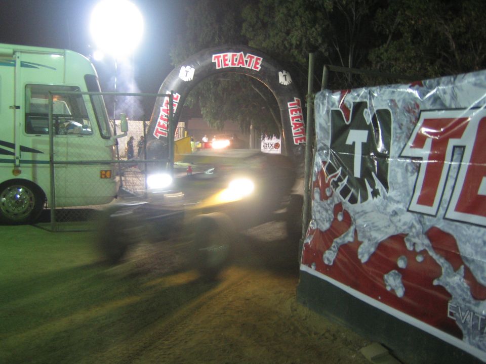 Motion-blurred vehicle passing a motorhome and Tecate banner at night