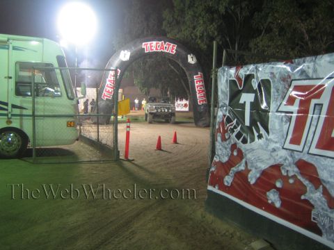 Truck on dirt course under a lit Tecate arch beside a motorhome
