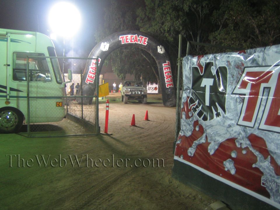 Truck on dirt course under a lit Tecate arch beside a motorhome