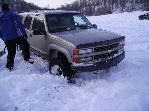 2000 Chevrolet Tahoe - A silver Chevrolet Tahoe is stuck in a snowy field, with a person attempting to dig it out.