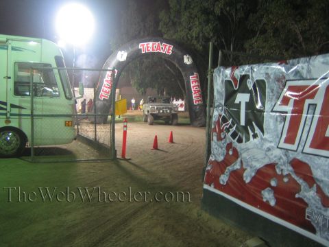 Pickup truck driving under a lit Tecate arch on a dirt course