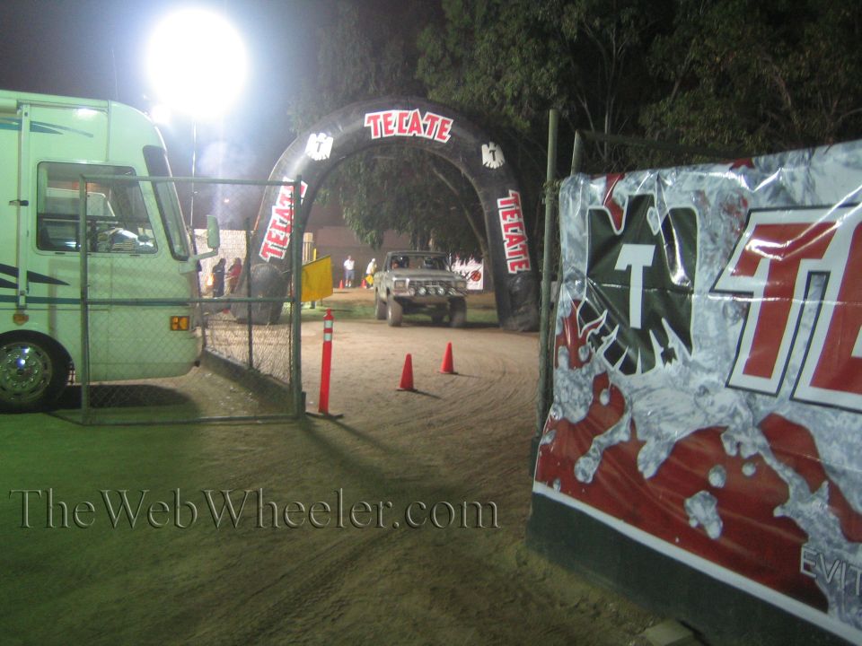 Pickup truck driving under a lit Tecate arch on a dirt course