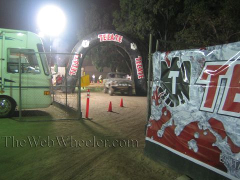 Pickup truck on dirt course under lit Tecate arch at night
