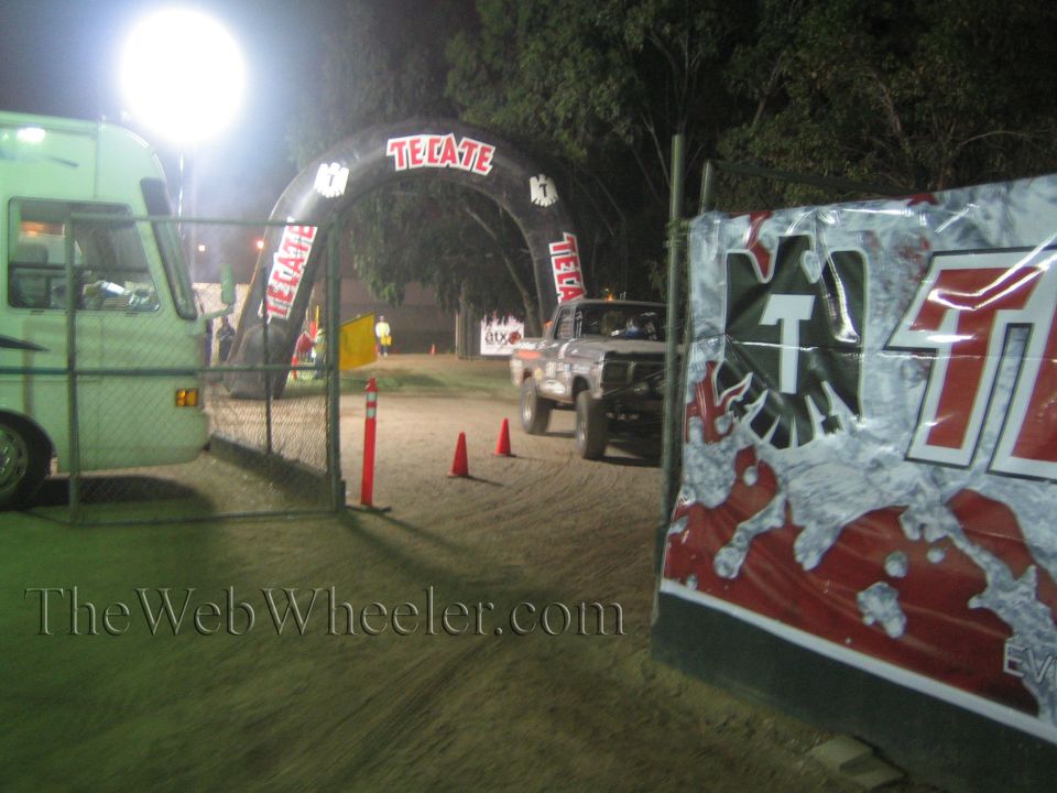 Lifted pickup truck on dirt course under lit Tecate arch at night