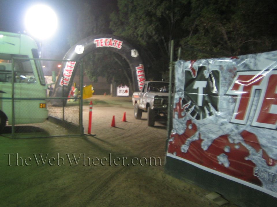 Lifted pickup truck entering dirt course under Tecate arch at night