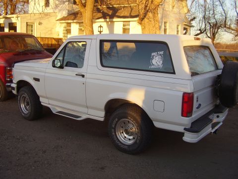 1995 Ford Bronco - A white Ford Bronco is parked next to a red truck in front of a house.