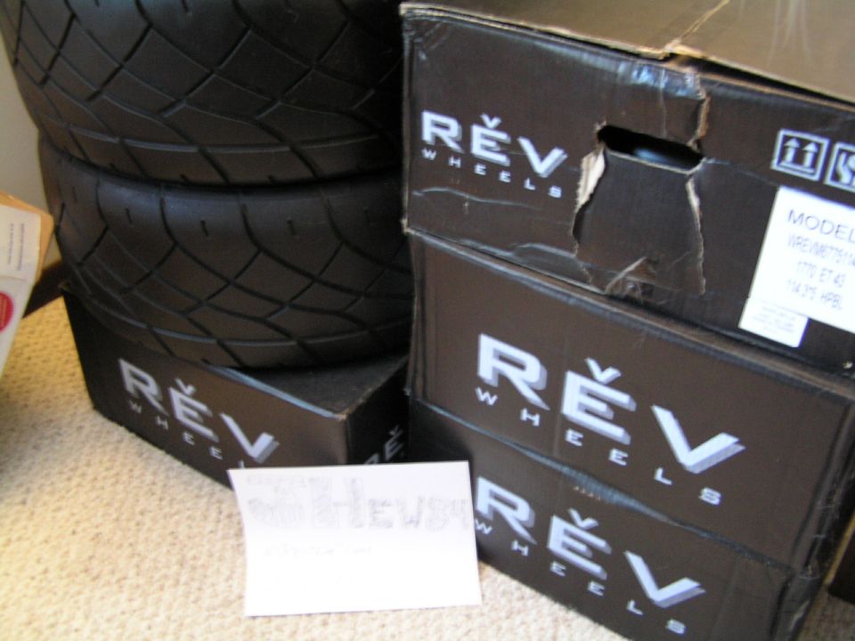 Stacked REV Wheels boxes and two tires with a handwritten note card on carpet.