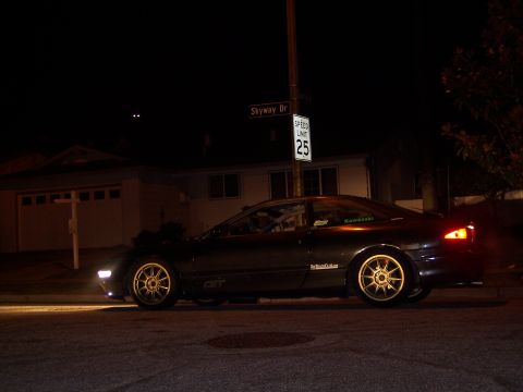 1995 Ford Probe - A dark coupe with gold rims is parked on a street at night, with a speed limit sign in the background.