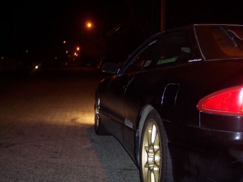1995 Ford Probe - A black coupe with gold rims is parked on a street at night, illuminated by streetlights and its own headlights.