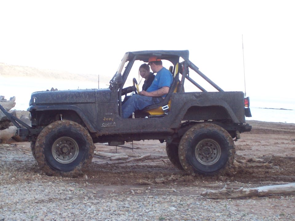 Two people sitting in a lifted Jeep Wrangler at a sandy beach