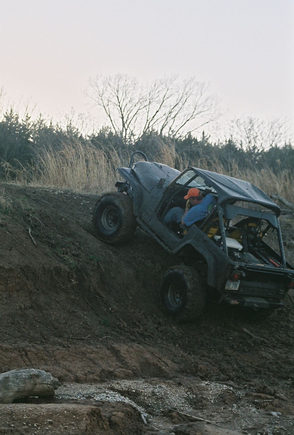 Black Jeep CJ climbing a dirt hill, driver wearing orange hat