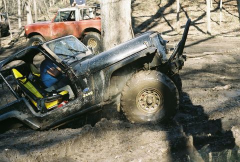 1981 Jeep CJ7 - A black 1981 Jeep CJ7 is stuck in thick mud, with a red SUV visible in the background.