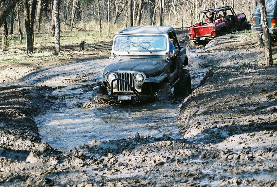 1981 Jeep CJ7 and other Jeeps navigating a muddy trail in a wooded area