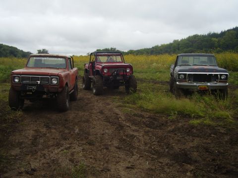 1981 Jeep CJ7 - Three off-road vehicles are parked in a muddy field under an overcast sky.