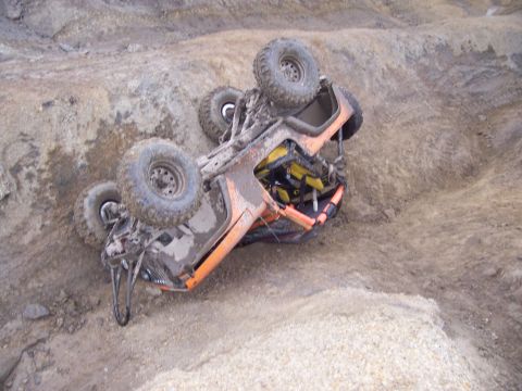 1981 Jeep CJ7 - An overturned orange off-road vehicle lies on its side in a dirt landscape, its wheels in the air.