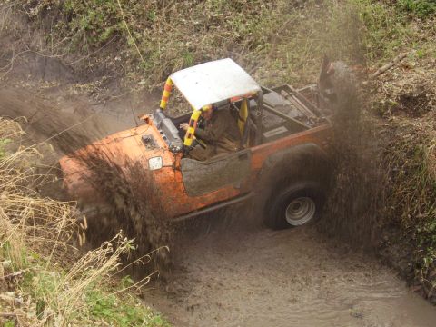1981 Jeep CJ7 - Orange Jeep CJ7 navigates a challenging muddy terrain, splashing water and mud.