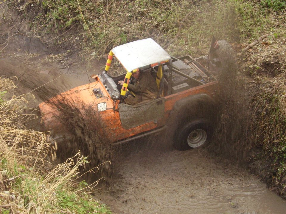 1981 Jeep CJ7 driving through a muddy ditch, kicking up water and dirt