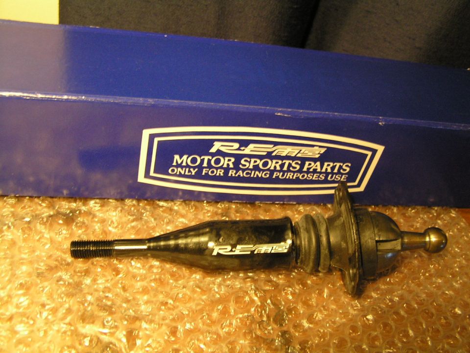 RE Amemiya short-throw shifter with rubber boot beside its blue racing-parts box