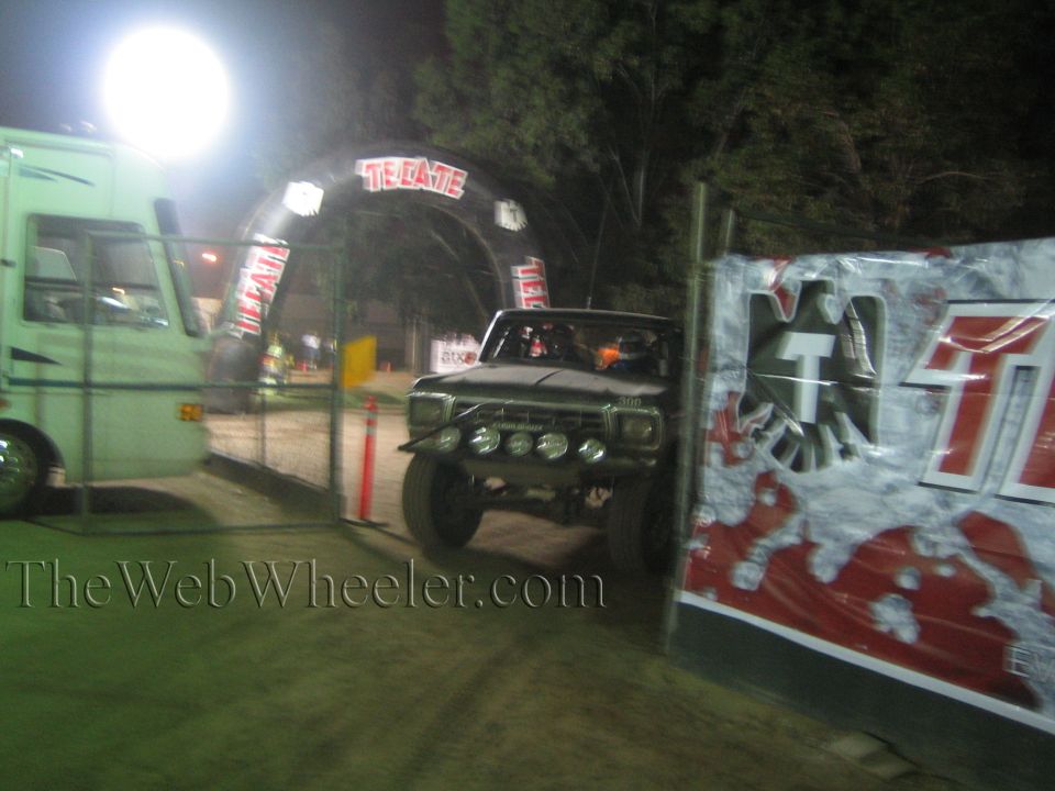 Front-light off-road truck on dirt course under Tecate arch at night
