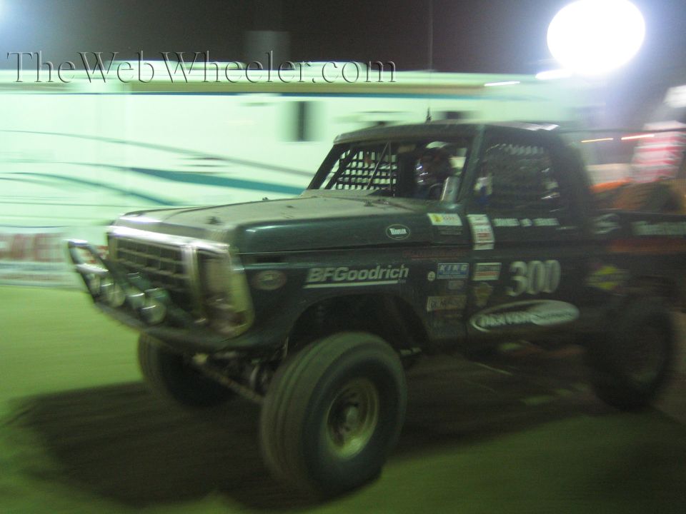 Green Ford off-road race truck number 300 with caged cab at night